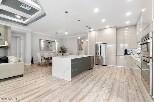 kitchen with an island with sink, appliances with stainless steel finishes, pendant lighting, and white cabinets