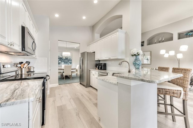 kitchen with a breakfast bar, white cabinetry, light stone counters, appliances with stainless steel finishes, and kitchen peninsula