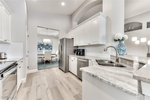 kitchen featuring sink, appliances with stainless steel finishes, light stone counters, white cabinets, and light wood-type flooring