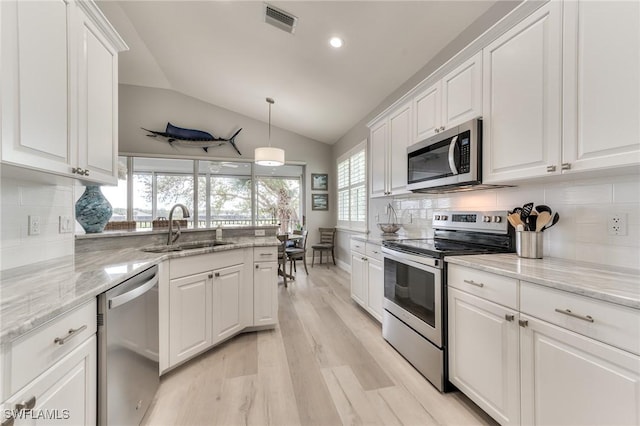 kitchen with appliances with stainless steel finishes, sink, white cabinets, hanging light fixtures, and light stone countertops