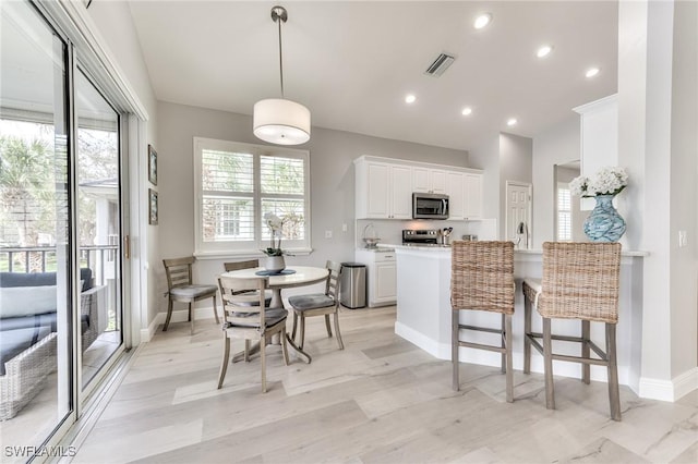 kitchen featuring white cabinetry, hanging light fixtures, stainless steel appliances, light stone countertops, and kitchen peninsula