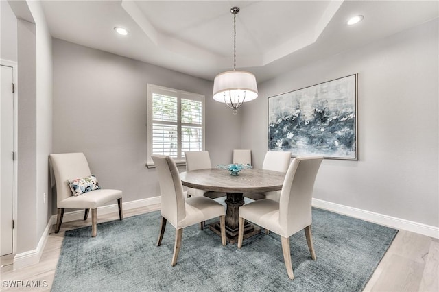 dining space with an inviting chandelier, a raised ceiling, and light wood-type flooring