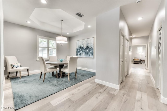 dining room with a raised ceiling and light wood-type flooring