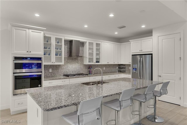 kitchen featuring white cabinetry, sink, a kitchen island with sink, stainless steel appliances, and wall chimney exhaust hood