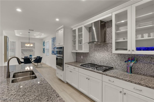 kitchen with wall chimney range hood, sink, stainless steel appliances, white cabinets, and a raised ceiling