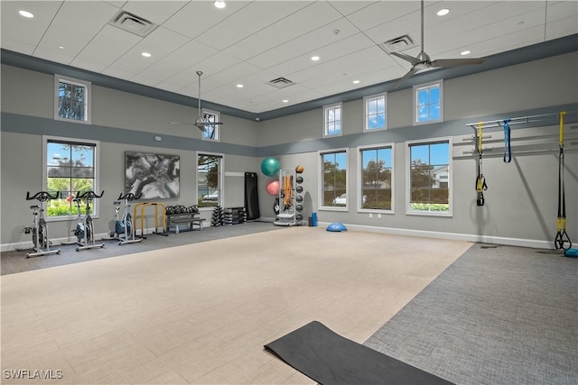 exercise room featuring a towering ceiling, light colored carpet, and ceiling fan