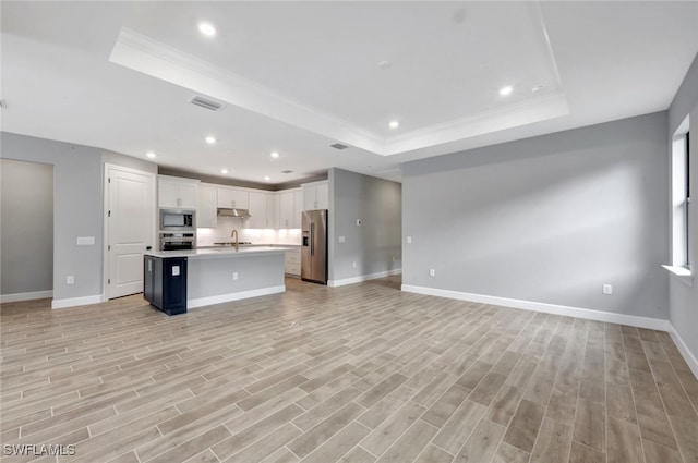 kitchen featuring sink, a tray ceiling, a kitchen island with sink, stainless steel appliances, and white cabinets