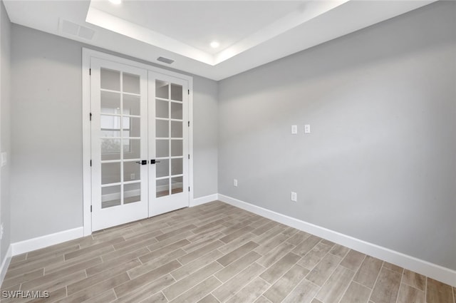 empty room with a raised ceiling, french doors, and light hardwood / wood-style floors