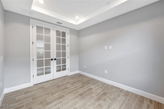 spare room with light hardwood / wood-style floors, a tray ceiling, and french doors