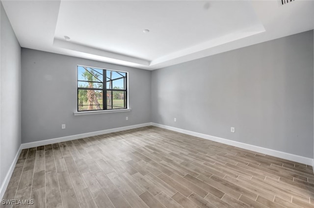 unfurnished room with light wood-type flooring and a tray ceiling