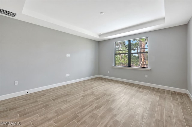 spare room featuring light wood-type flooring and a raised ceiling