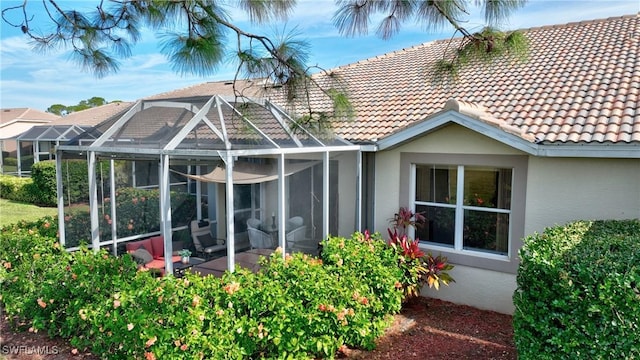 back of house featuring a tile roof, a lanai, and stucco siding