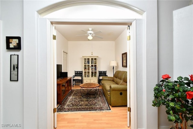 living area featuring light wood-style floors, ceiling fan, and arched walkways