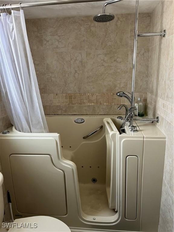 bathroom with a combined bath / shower with jetted tub, toilet, and tile walls