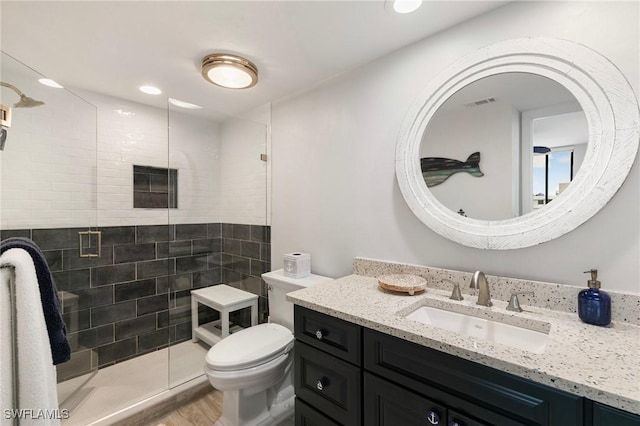 bathroom with toilet, wood-type flooring, tiled shower, and vanity