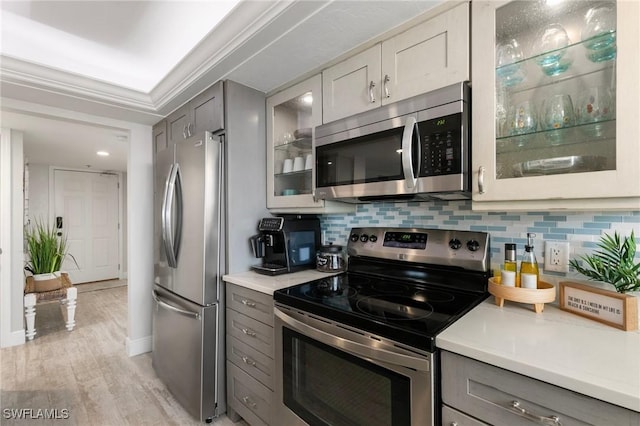 kitchen with appliances with stainless steel finishes, decorative backsplash, gray cabinets, ornamental molding, and light wood-type flooring