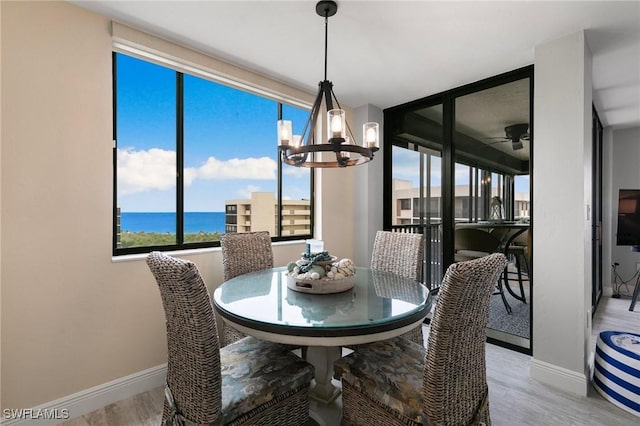 dining space featuring light wood-type flooring, ceiling fan with notable chandelier, and a water view