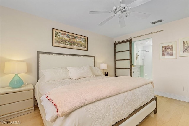 bedroom featuring ceiling fan, a barn door, ensuite bathroom, and light hardwood / wood-style floors