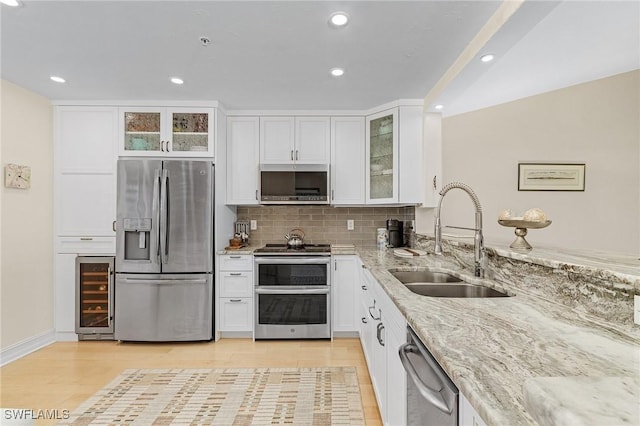 kitchen featuring sink, appliances with stainless steel finishes, light stone counters, white cabinets, and beverage cooler