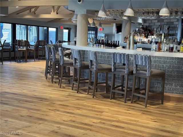 bar featuring hanging light fixtures and light hardwood / wood-style flooring