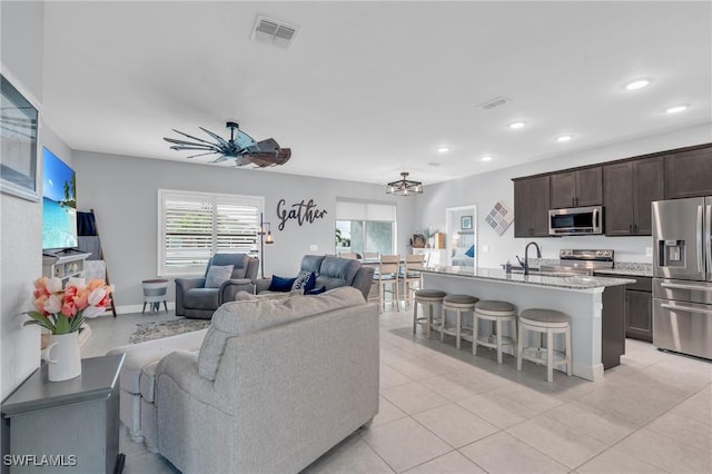 tiled living room featuring ceiling fan with notable chandelier and sink