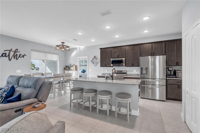 kitchen featuring light stone countertops, stainless steel appliances, sink, a center island with sink, and a breakfast bar area