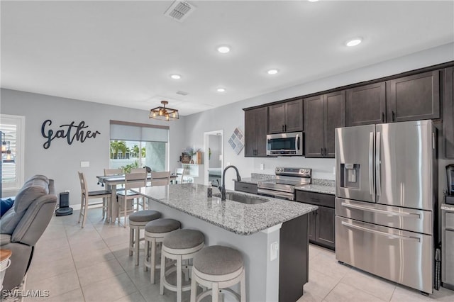 kitchen with a center island with sink, stainless steel appliances, dark brown cabinets, light stone countertops, and sink