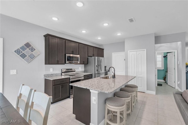 kitchen with light tile patterned floors, a center island with sink, appliances with stainless steel finishes, a kitchen breakfast bar, and sink