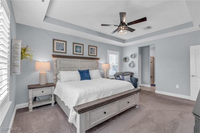 bedroom with ceiling fan, light carpet, and a tray ceiling