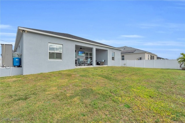 back of property with ceiling fan, a patio area, and a yard