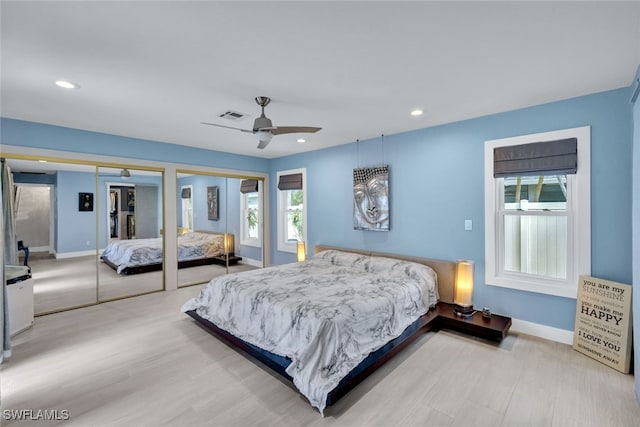 bedroom with multiple windows, two closets, light hardwood / wood-style flooring, and ceiling fan