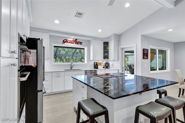 kitchen with sink, a breakfast bar area, white cabinetry, stainless steel appliances, and a center island