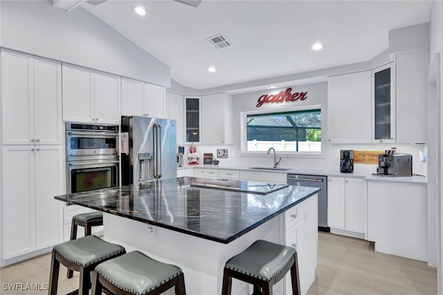 kitchen with sink, a breakfast bar, white cabinetry, stainless steel appliances, and a kitchen island