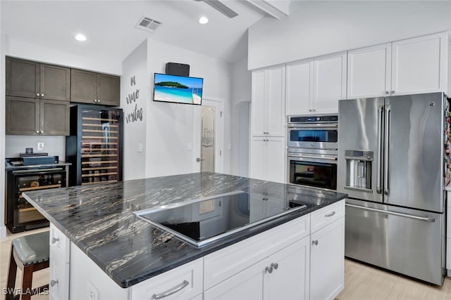 kitchen featuring appliances with stainless steel finishes, a kitchen island, dark stone counters, beverage cooler, and white cabinets