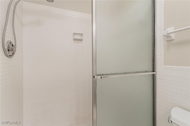 bathroom featuring tile walls, a shower with door, and toilet