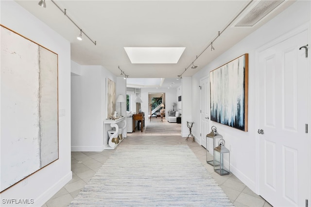 hallway featuring light tile patterned floors, a skylight, and track lighting