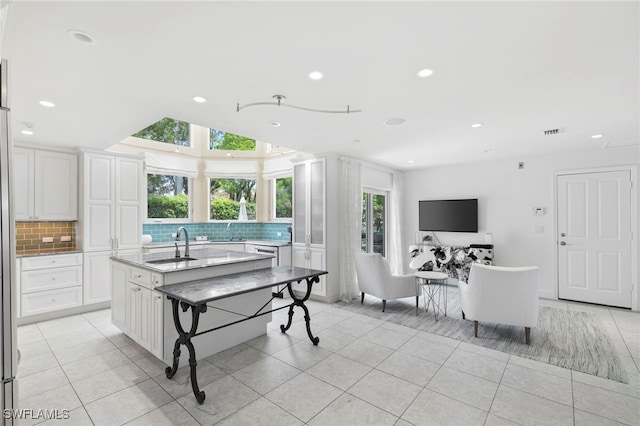 interior space with sink, light tile patterned floors, an island with sink, and white cabinets