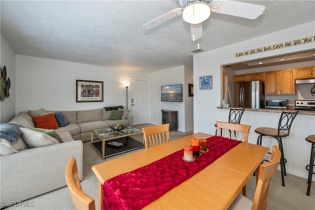 dining space featuring ceiling fan, light colored carpet, and a textured ceiling