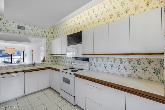 kitchen with white appliances, white cabinetry, light tile patterned floors, sink, and an inviting chandelier