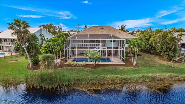 rear view of house with glass enclosure, a water view, and a yard