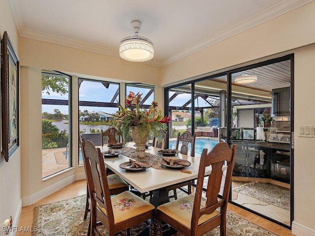 dining room with crown molding, a water view, light hardwood / wood-style flooring, and a wealth of natural light