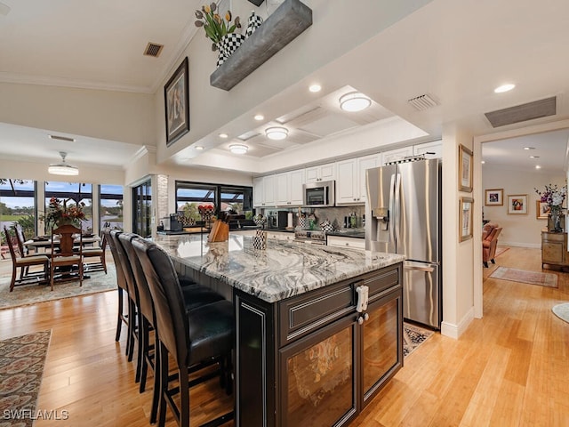 kitchen with white cabinets, a center island, a kitchen bar, stainless steel appliances, and light hardwood / wood-style flooring