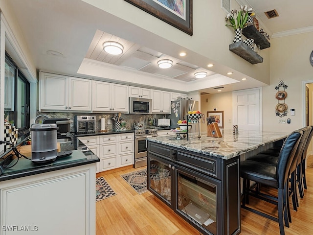 kitchen featuring a center island, white cabinetry, a raised ceiling, ornamental molding, and stainless steel appliances