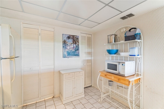 kitchen with light tile patterned flooring, white appliances, and a drop ceiling