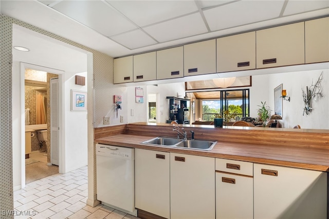 kitchen with dishwasher, wood counters, sink, a drop ceiling, and cream cabinetry