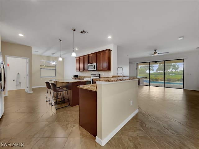 kitchen with ceiling fan, appliances with stainless steel finishes, light stone countertops, pendant lighting, and a breakfast bar