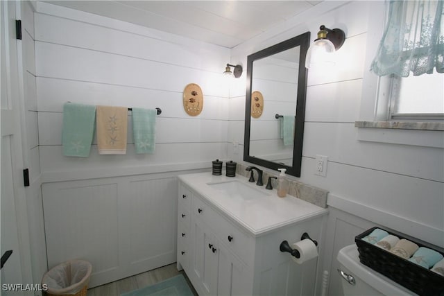 bathroom with vanity, wooden walls, and toilet