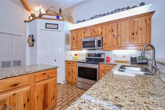 kitchen featuring light stone countertops, sink, backsplash, and appliances with stainless steel finishes