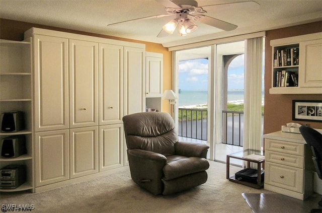 sitting room featuring a water view, light colored carpet, and ceiling fan