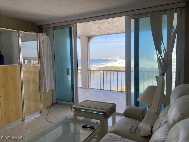 tiled living room featuring a textured ceiling, a wall of windows, a beach view, and a water view